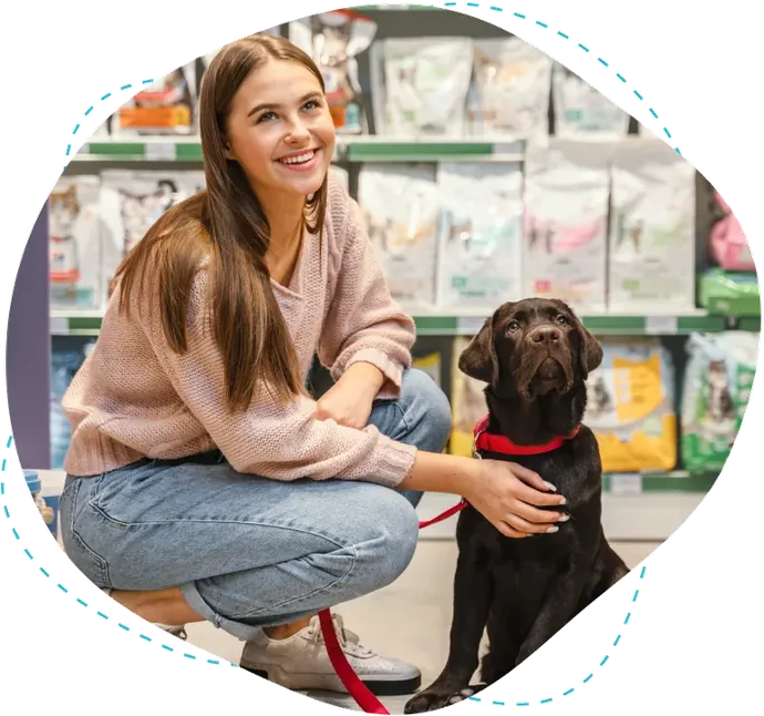 Chica en una tienda de mascotas agachada junto a su labrador negro
